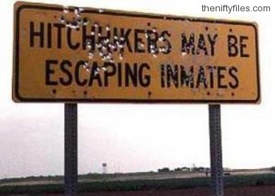 Sign reads 'hitchhikers may be escaping inmates'. Sign is full of bullet holes